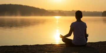 Person meditating by a calm lake at sunrise, symbolizing resilience and inner peace.